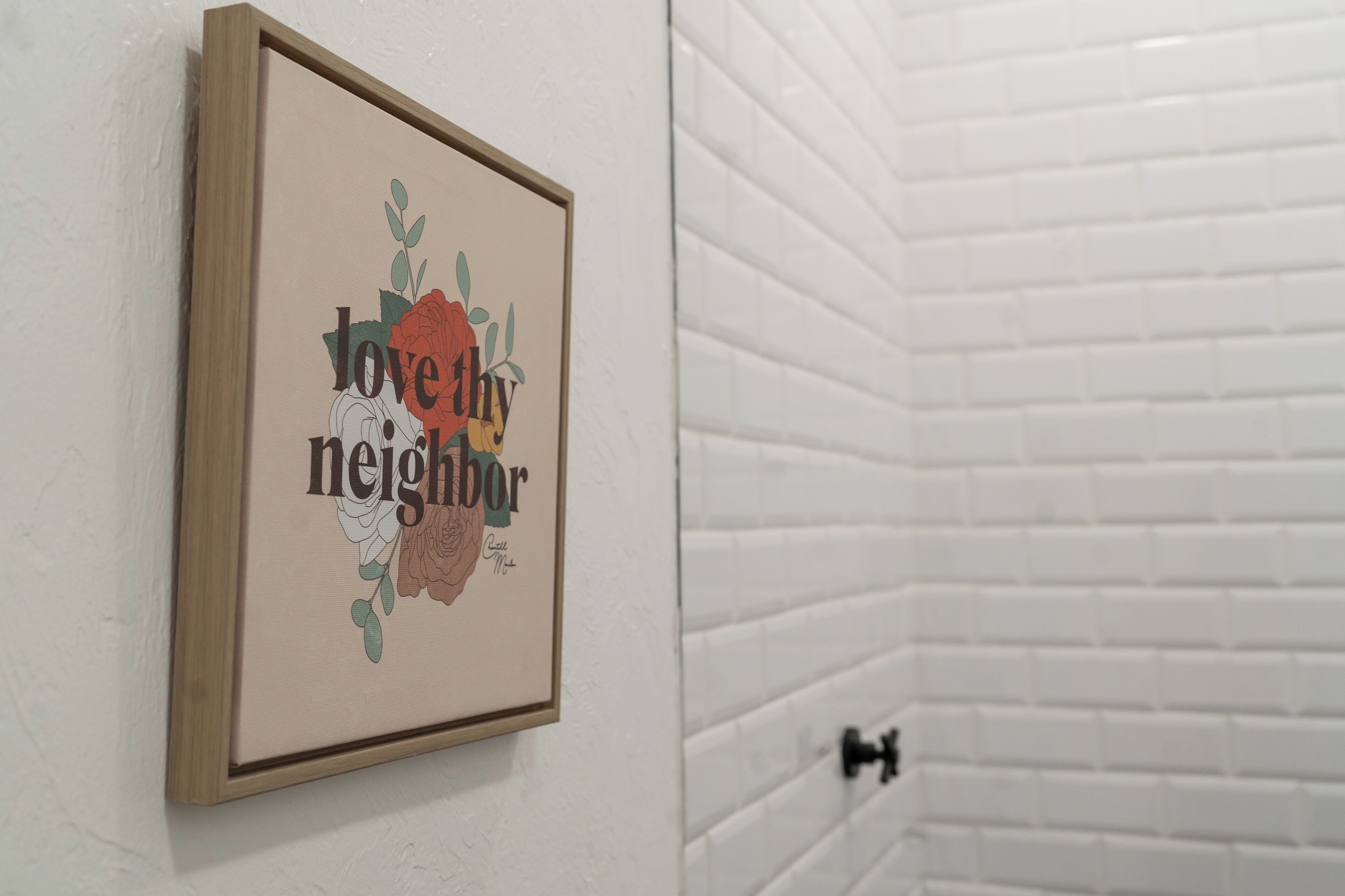 A framed artwork with the text "love thy neighbor" on a white wall.