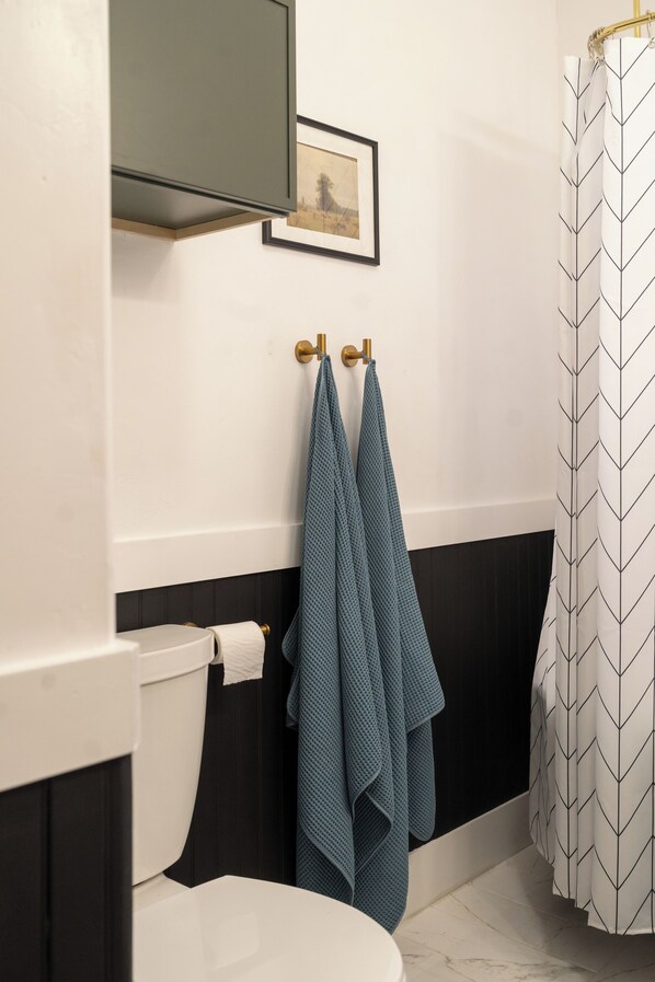 A bathroom with a toilet, a towel rack with two towels, a framed picture on the wall, and a shower curtain with a chevron pattern. - Large 2bd 2ba beautiful home in historical neighborhood center to everything. (Oklahoma City)