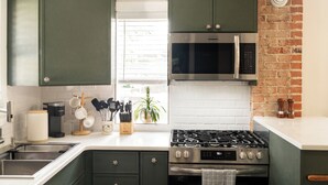 Uma cozinha moderna com armários verdes, eletrodomésticos de aço inoxidável e uma parede de tijolos decorativa.