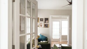 Um quarto com uma porta grande aberta, um sofá verde, uma mesinha e quadros nas paredes.