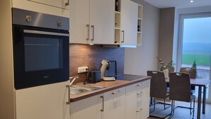 Een moderne keuken met een inbouwoven, een koffieapparaat en een eethoek met een tafel en stoelen.