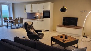 Een moderne woonkamer met een bank, een salontafel, een televisie, en een keukenhoek met kasten en een eethoek.