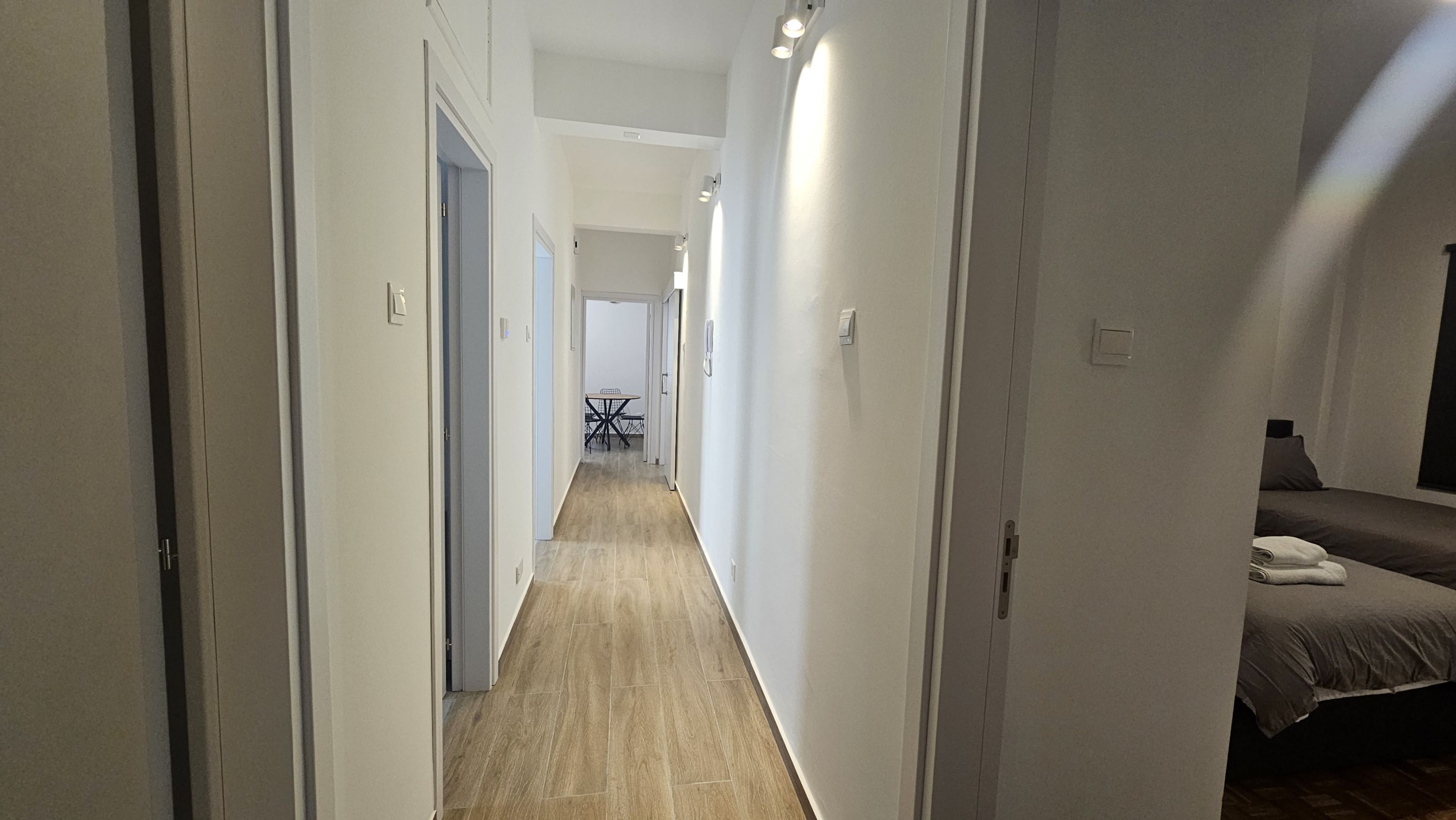 A narrow hallway with wooden flooring leading to a dining area with a table and chairs.