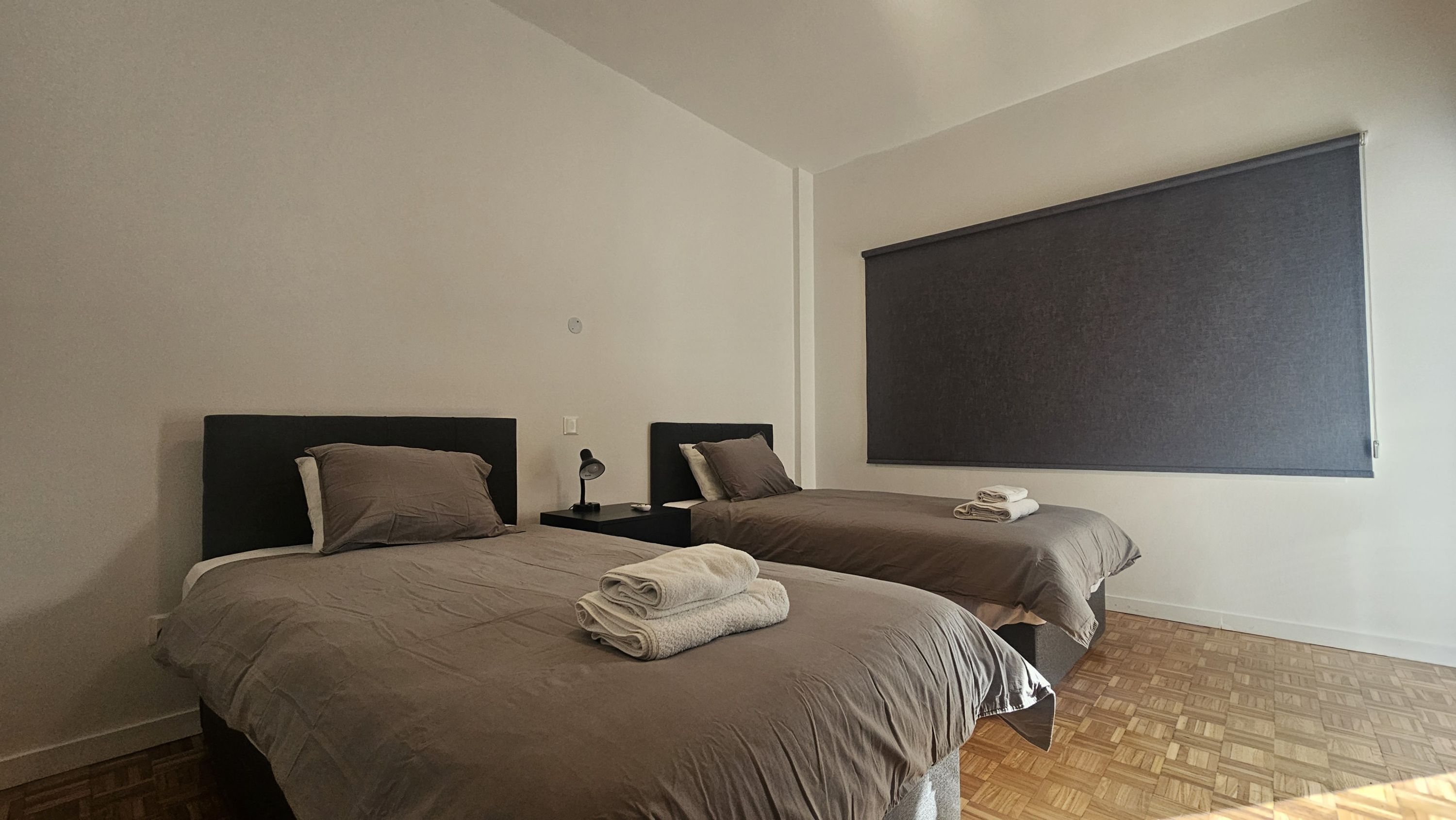 A hotel room with two beds, each with a headboard, a large window, and a wooden floor.