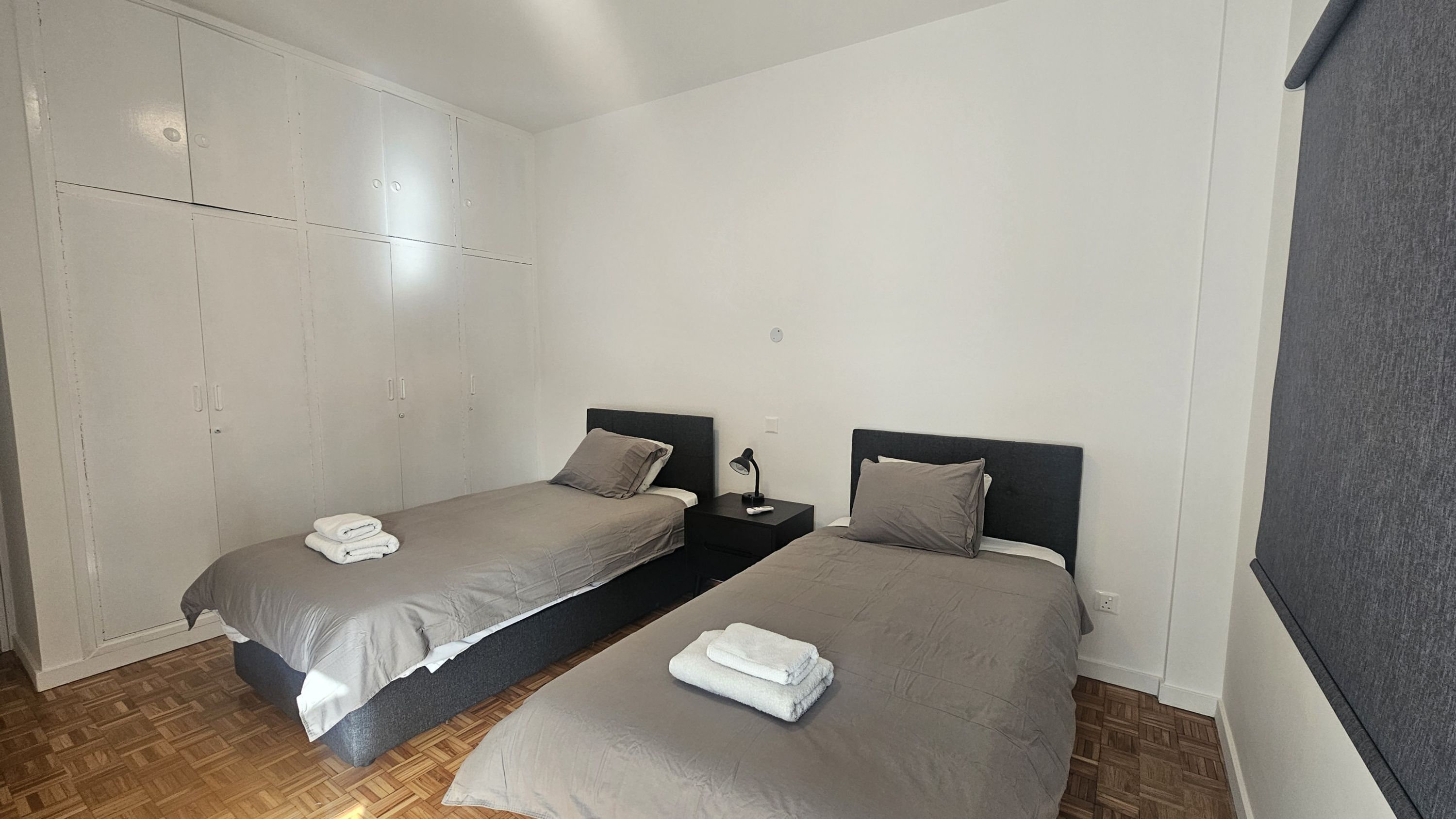 Un dormitorio con dos camas individuales, un armario y una mesita de noche con lámpara.