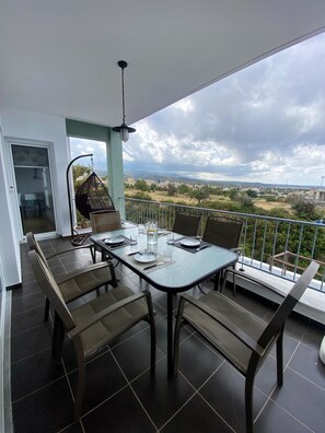 A balcony with a dining table set for four, chairs, and a hanging chair.