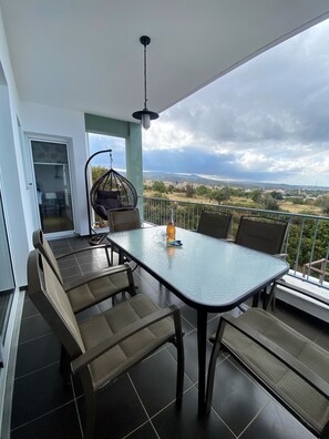 A balcony with a glass table and chairs, a hanging chair, and a view of the landscape.