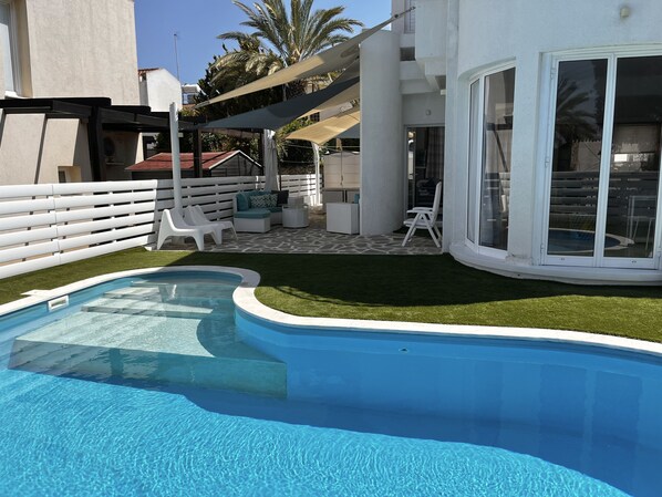 A swimming pool with a white deck, a covered seating area, and a white fence.