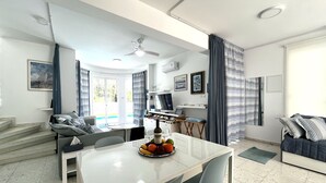 Un soggiorno moderno con zona pranzo, caratterizzato da un tavolo bianco, sedie grigie, un divano e un televisore.