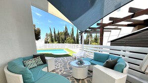 Un'area salotto esterna coperta con mobili in vimini e vista su una piscina.