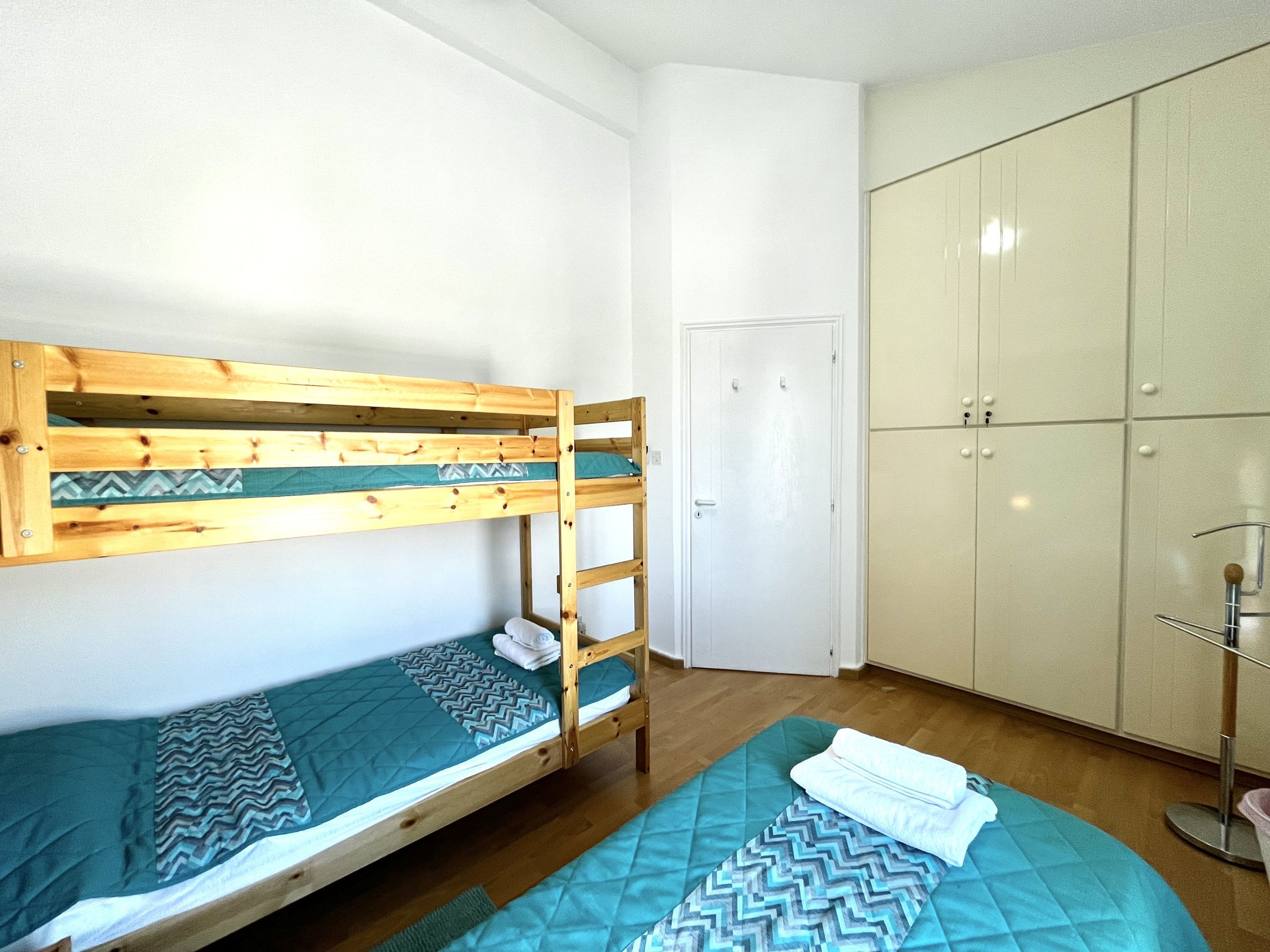 Una cama individual superpuesta con ropa de cama estampada, un armario con varias puertas y una puerta al fondo.