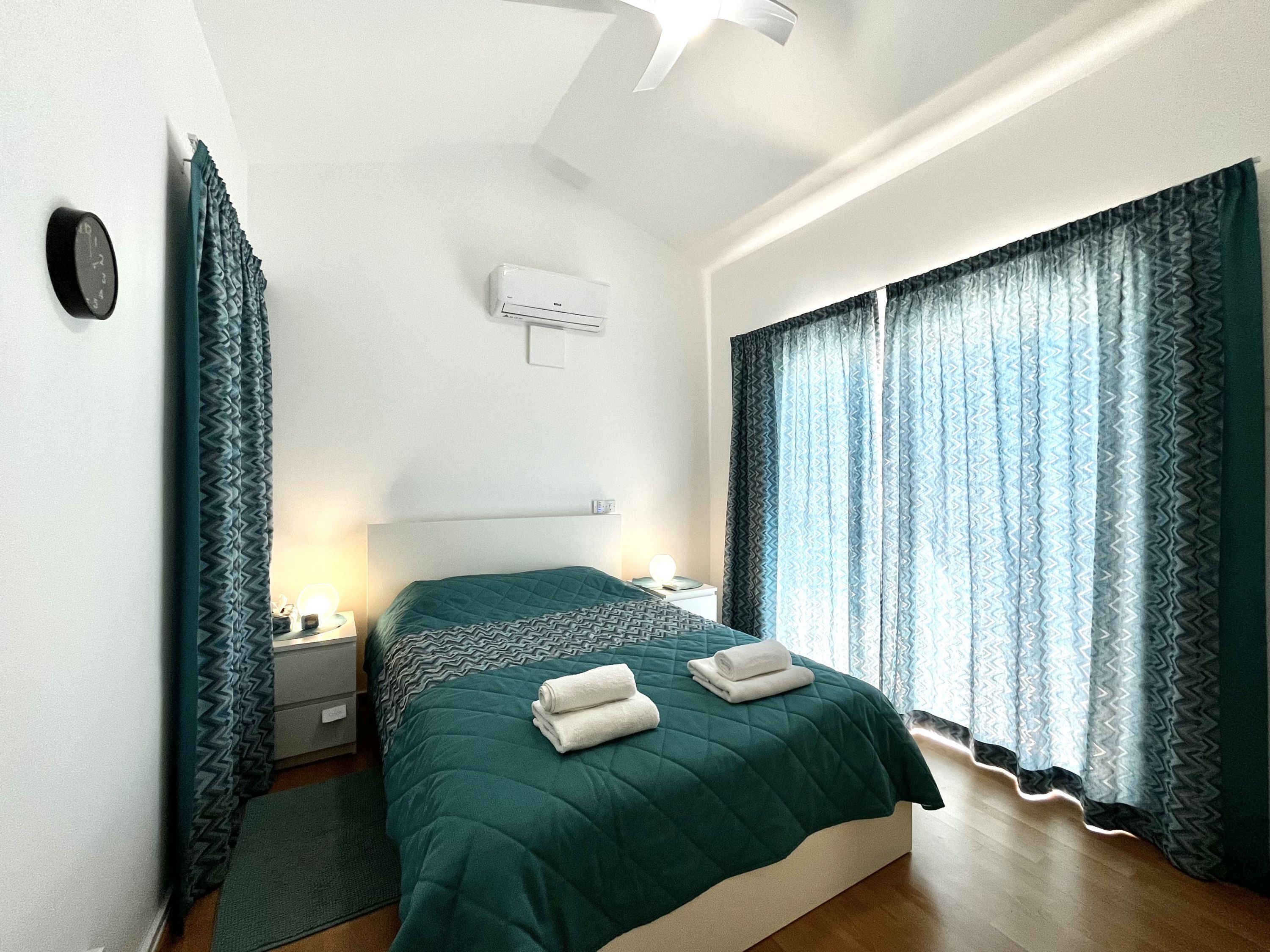Un dormitorio moderno con cama, mesitas de noche, un equipo de aire acondicionado y cortinas estampadas.