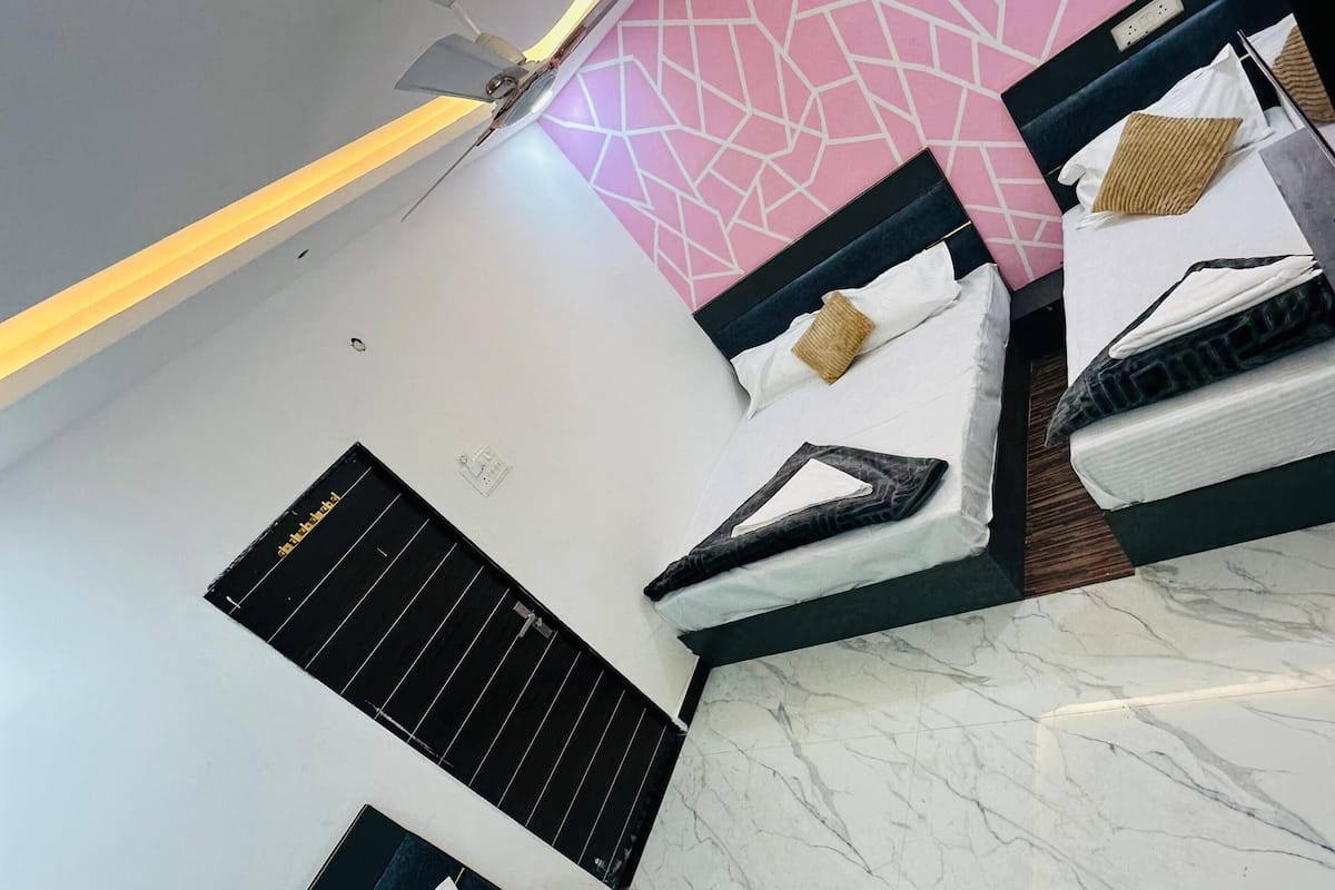 A hotel room with three beds, a geometric patterned wall, a ceiling light, and a window with a black grill.