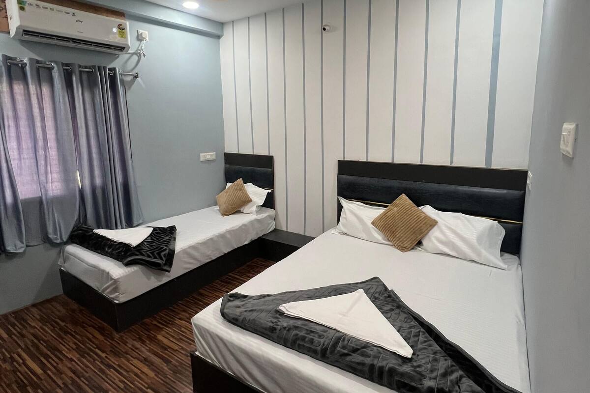 A hotel room with two beds, a ceiling fan, an air conditioning unit, and a wooden floor.