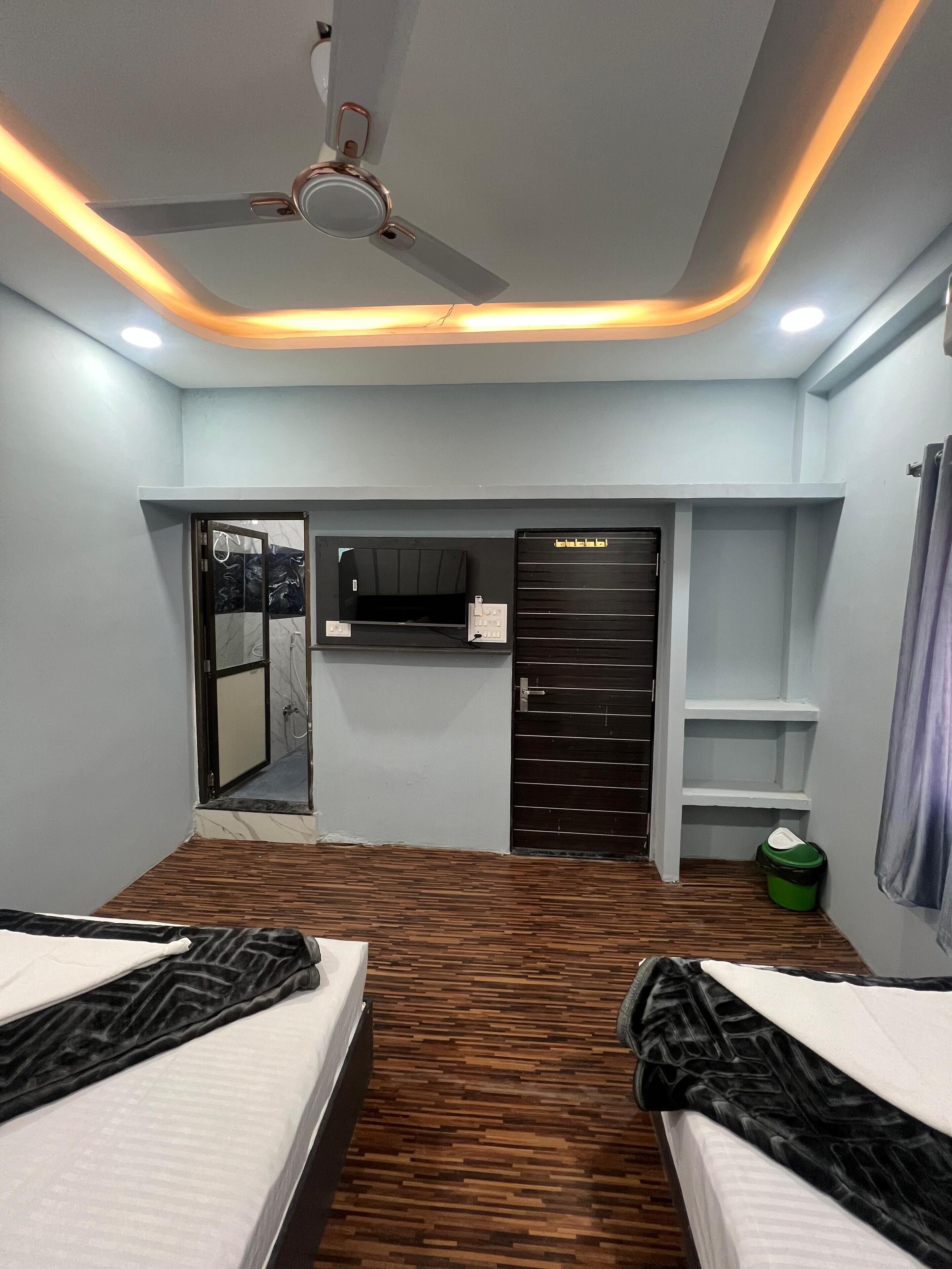 A hotel room with two beds, a ceiling fan, a wardrobe, a mirror, and a shower area.