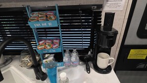 A coffee station with a coffee maker, water bottles, a mug, and a sign about coffee and hot chocolate.