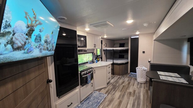 Une cuisine compacte pour camping-car, équipée d’une cuisinière, d’un four à micro-ondes et d’un évier, ainsi que d’un petit coin repas et d’un lit superposé.