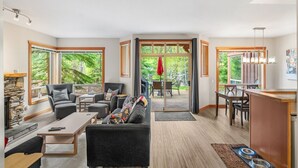 Un vaste espace de vie doté d’une cheminée, de sièges confortables, d’un coin repas et de grandes fenêtres offrant une vue sur l’extérieur.