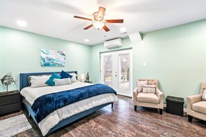 Primary Suite - Spacious king bedroom with mint green walls, navy upholstered bed, teal velvet throw, abstract art, and a seating area. - Lakefront Retreat, Pool, Boat Dock, Hot Tub (Bumpass)