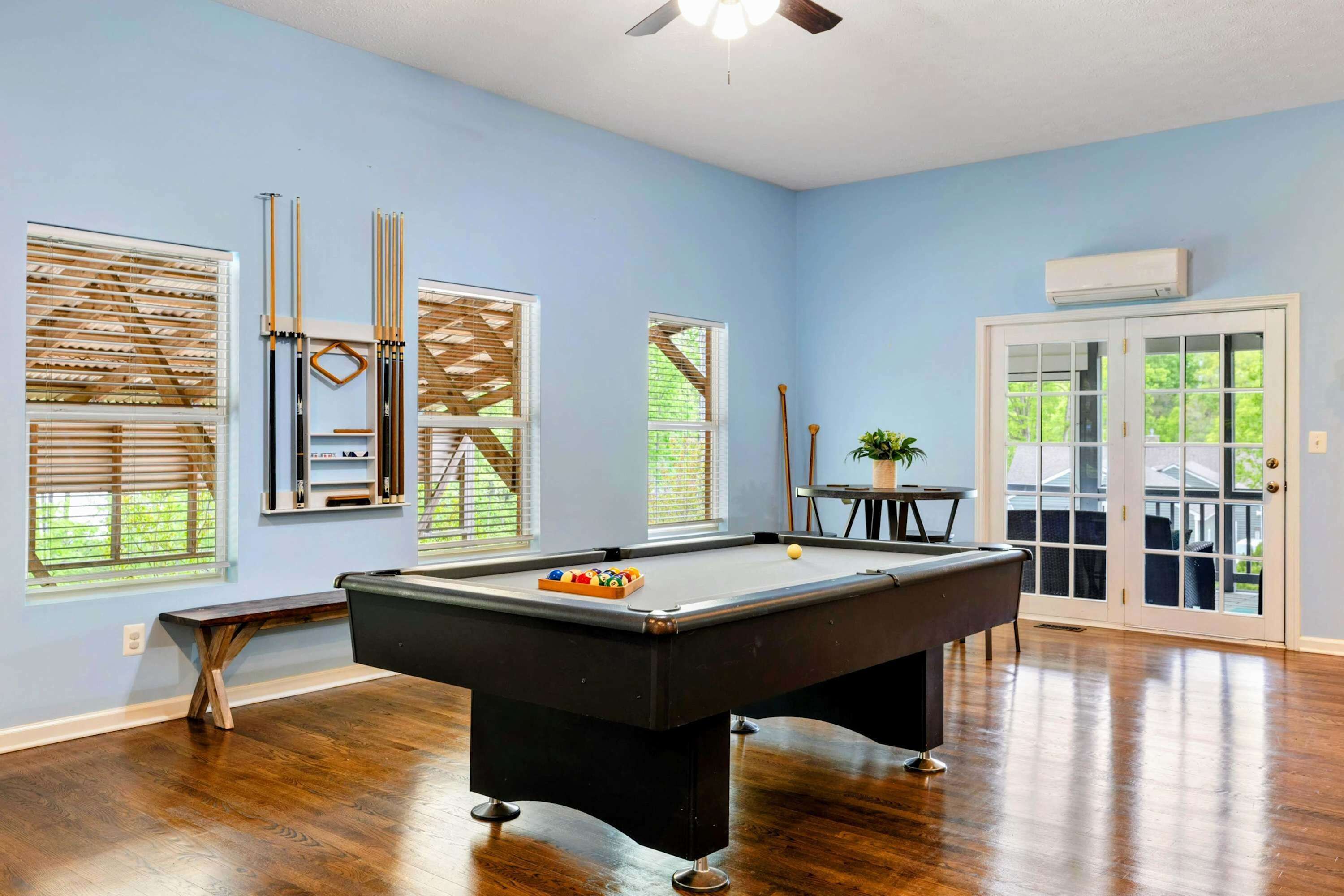 A pool table in a room with blue walls, wooden flooring, and a ceiling fan.