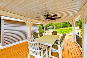A covered patio with a table and chairs, a ceiling fan, and a view of a house and greenery. - Lakefront Retreat, Pool, Boat Dock, Hot Tub (Bumpass)
