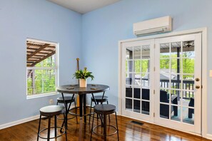 A room with a round table, four chairs, a potted plant, a window with blinds, and a door with glass panels.