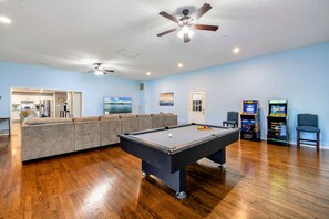 A room with a pool table, a ceiling fan, a sofa, and arcade games.
