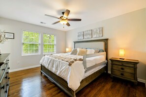 A bedroom with a bed, a nightstand, a ceiling fan, and a window with blinds.