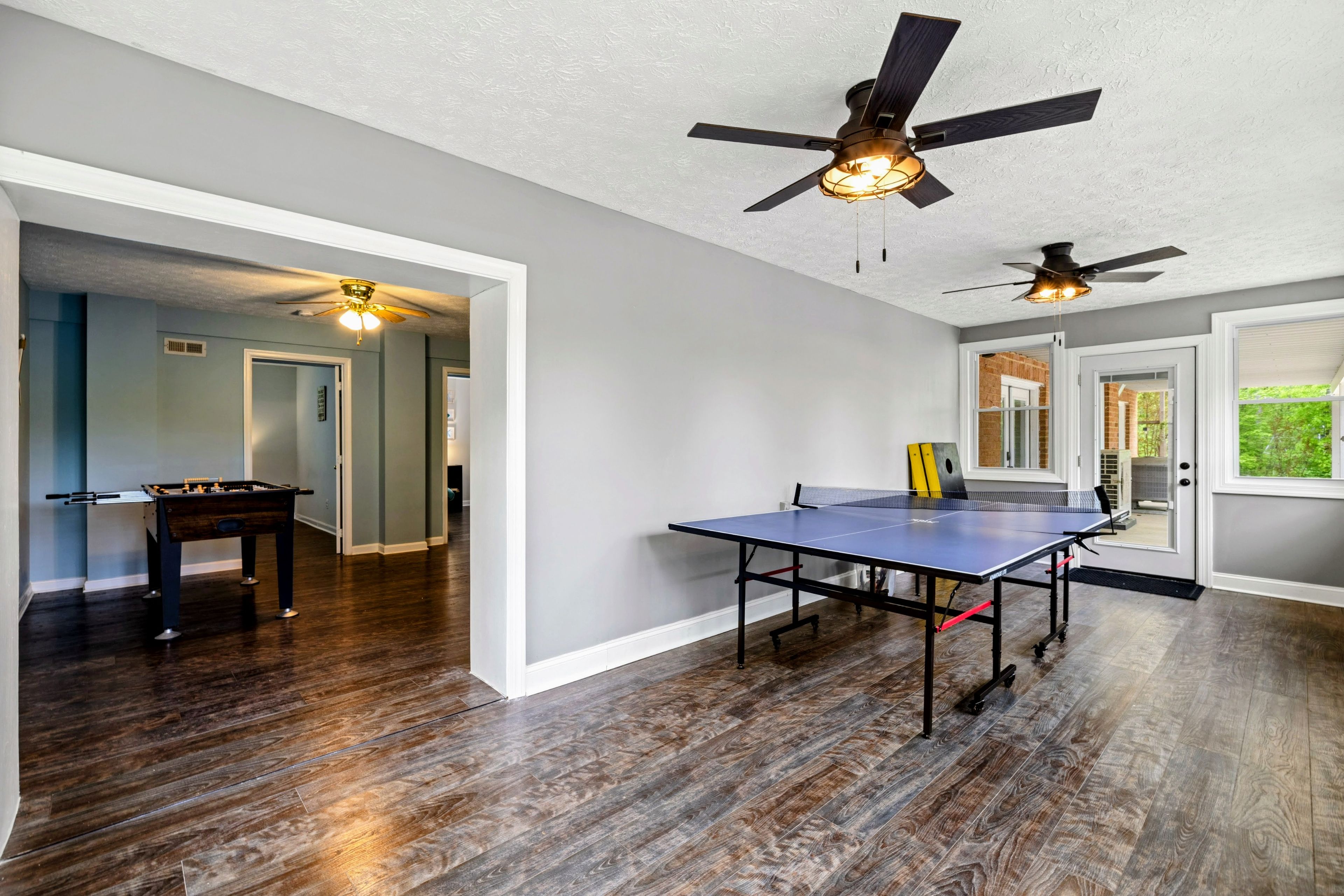 Una habitación amplia con mesa de ping pong, mesa de fútbol de mesa y dos ventiladores de techo.