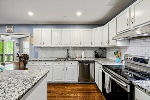 A modern kitchen with white cabinets, a stainless steel dishwasher, a black stove, and a granite countertop. - Lakefront Retreat, Pool, Boat Dock, Hot Tub (Bumpass)