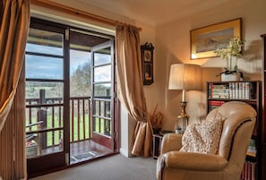 A room with a large window, a leather chair, a bookshelf, and a clock on the wall.