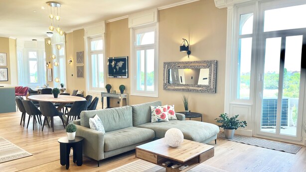 A spacious living room with a large sectional sofa, a coffee table, and a dining area with a round table and chairs.