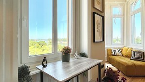 A room with a large window, a wooden table, a bench, and a sofa with cushions.