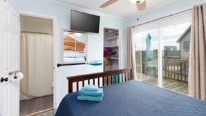 Ein Schlafzimmer mit Bett, Deckenventilator, Fernseher, einer Schiebetür zu einem Balkon und Holzboden.