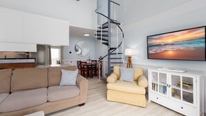 Ein modernes Wohnzimmer mit hoher Decke, einer Wendeltreppe, einem Flachbildfernseher und einem Essbereich.