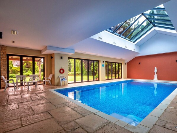 Una piscina interior con tragaluces, suelo de piedra y vistas al exterior.