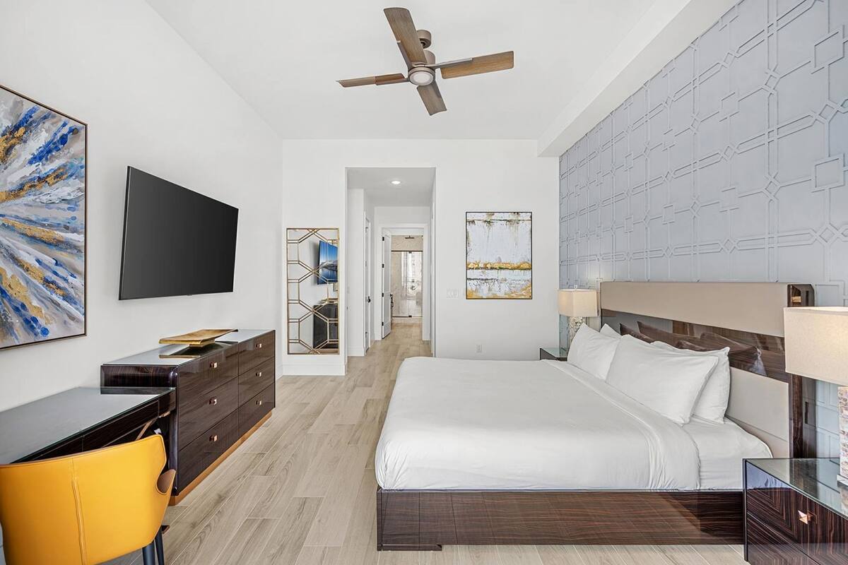 Une chambre d’hôtel moderne, dotée d’un grand lit, d’un bureau avec une chaise, d’un ventilateur de plafond et d’œuvres d’art accrochées aux murs.