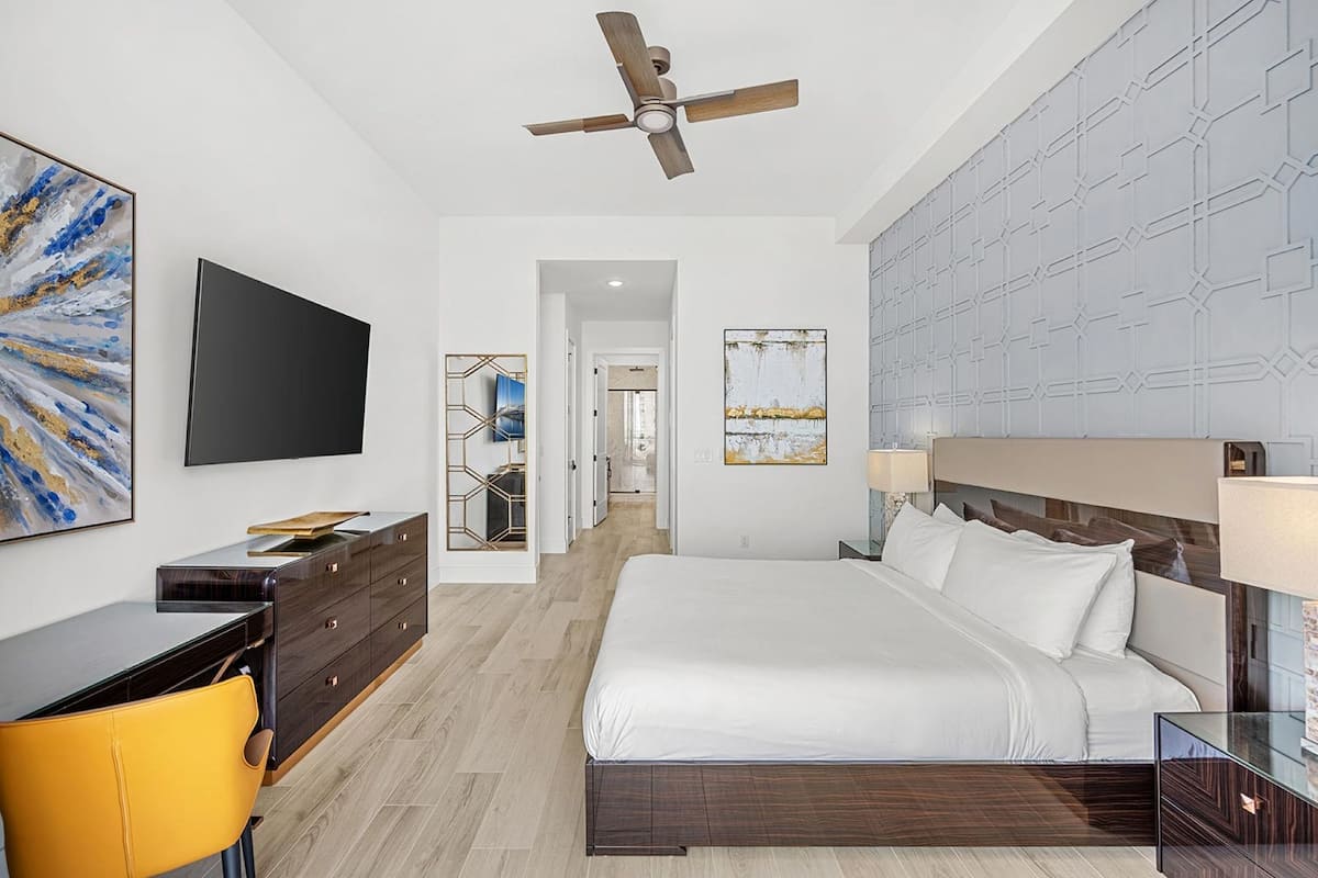 Ein modernes Hotelzimmer mit einem großen Bett, einem Schreibtisch mit Stuhl, einem Deckenventilator und Kunstwerken an den Wänden.