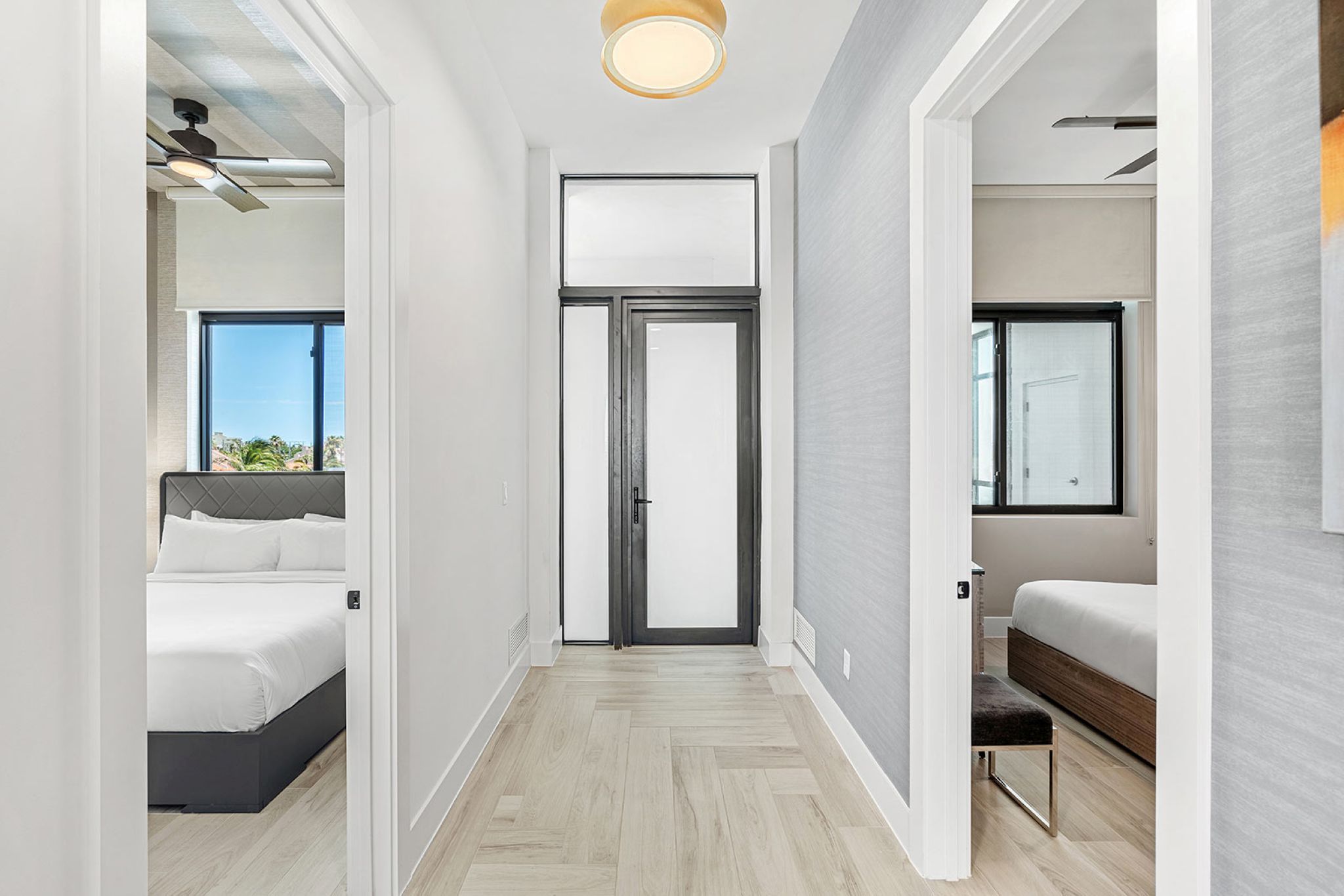 Habitació d'hotel moderna amb un llit, una banca, una porta i vista a l'exterior.
