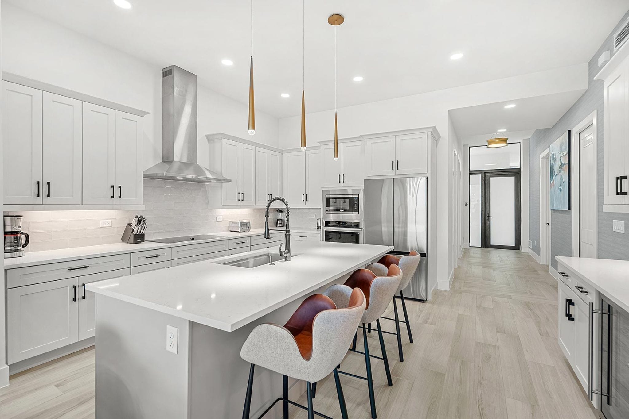 A modern kitchen with white cabinetry, a large island with bar stools, stainless steel appliances, and pendant lighting.
