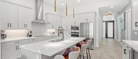 A modern kitchen with white cabinetry, a large island with bar stools, stainless steel appliances, and pendant lighting.