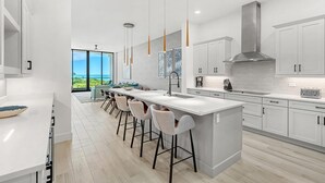 A modern kitchen with a large island, bar stools, pendant lighting, and a view of the outdoors. - Villatel At Harbor Island Beach Club (Melbourne Beach)