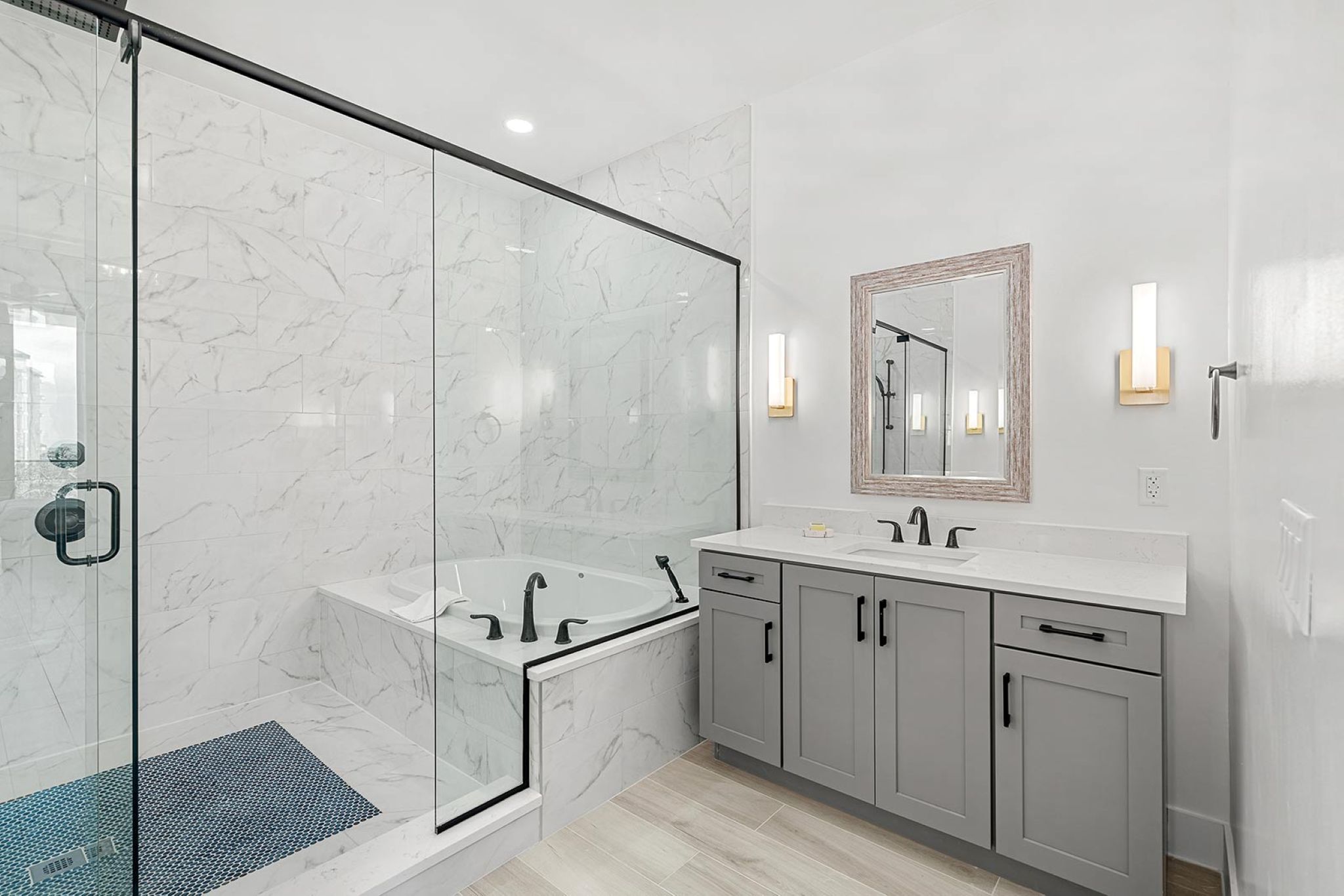 A modern bathroom with a glass-enclosed shower, a freestanding bathtub, and a vanity with a mirror and light fixtures.