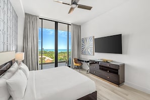 Habitación de hotel con cama, escritorio, silla, televisor y vista al océano.