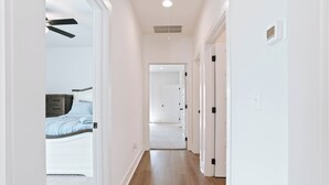 A hallway with a wooden floor, white walls, and a ceiling fan. There is a bed with a blue bedspread in the background. - Charming 2-bedroom townhome with WiFi and AC in Auburn (Auburn)