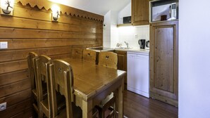 A wooden dining table with four chairs, a white dishwasher, and wooden cabinets in a kitchen. - Apartment in Modane Near Ski Slopes (Modane)