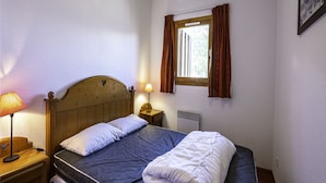 A single bed with a wooden headboard, a bedside table with a lamp, a window with curtains, and a wall-mounted picture. - Apartment in Modane Near Ski Slopes (Modane)