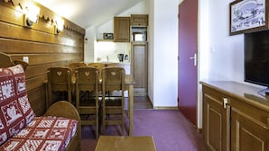 A cozy living room with a wooden sofa, a dining table with chairs, a kitchen area with cabinets, and a television on the wall. - Apartment in Modane Near Ski Slopes (Modane)