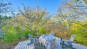 Eine Holzterrasse mit Adirondack-Stühlen und einem überdachten Tisch.