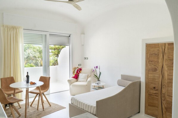 Une chambre moderne avec un lit, un coin salon avec des fauteuils, une petite table et une fenêtre avec des stores.